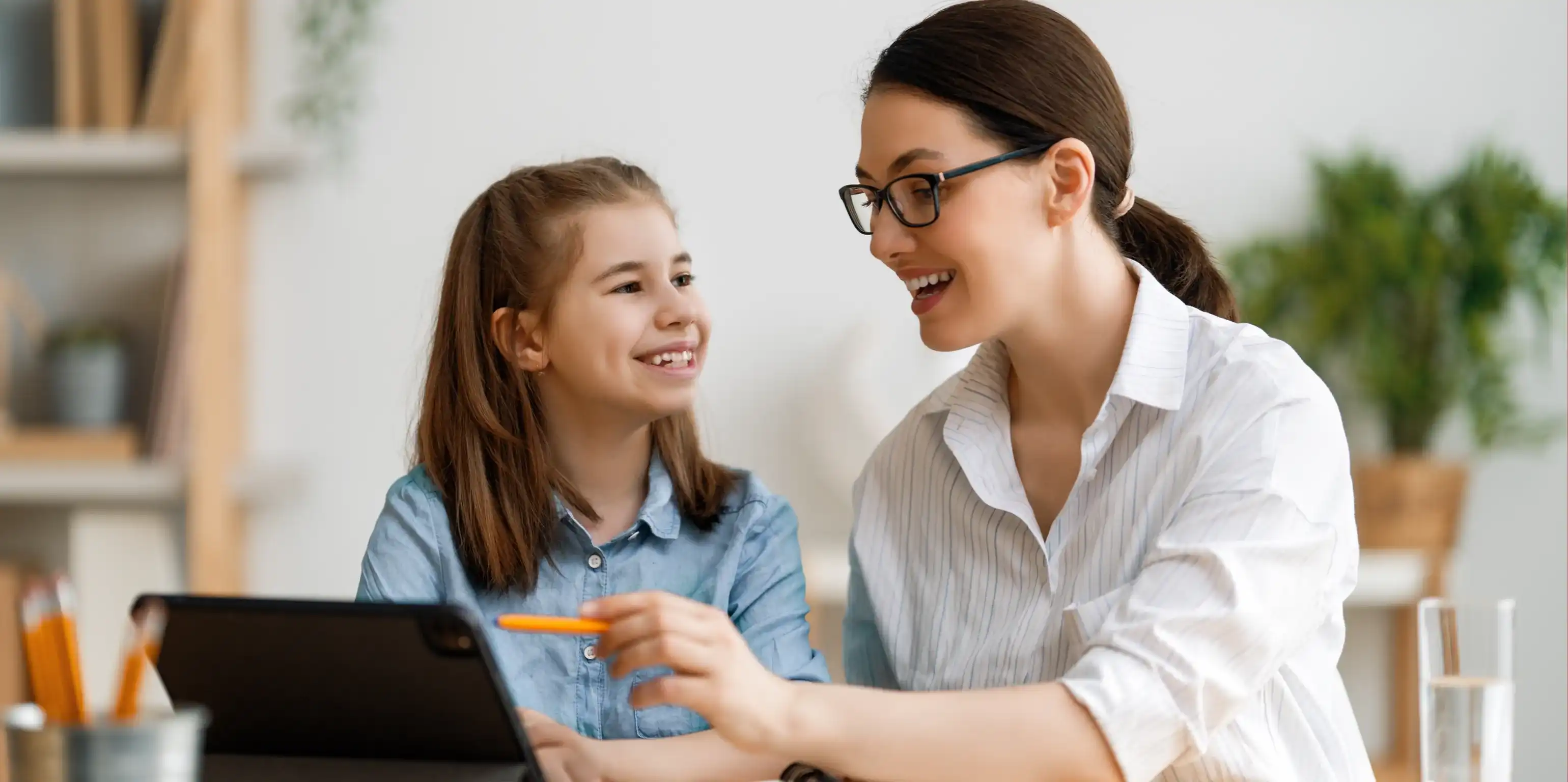 Una donna indica con una penna un iPad per spiegare qualcosa, accanto a lei una bambina siede sorridendo