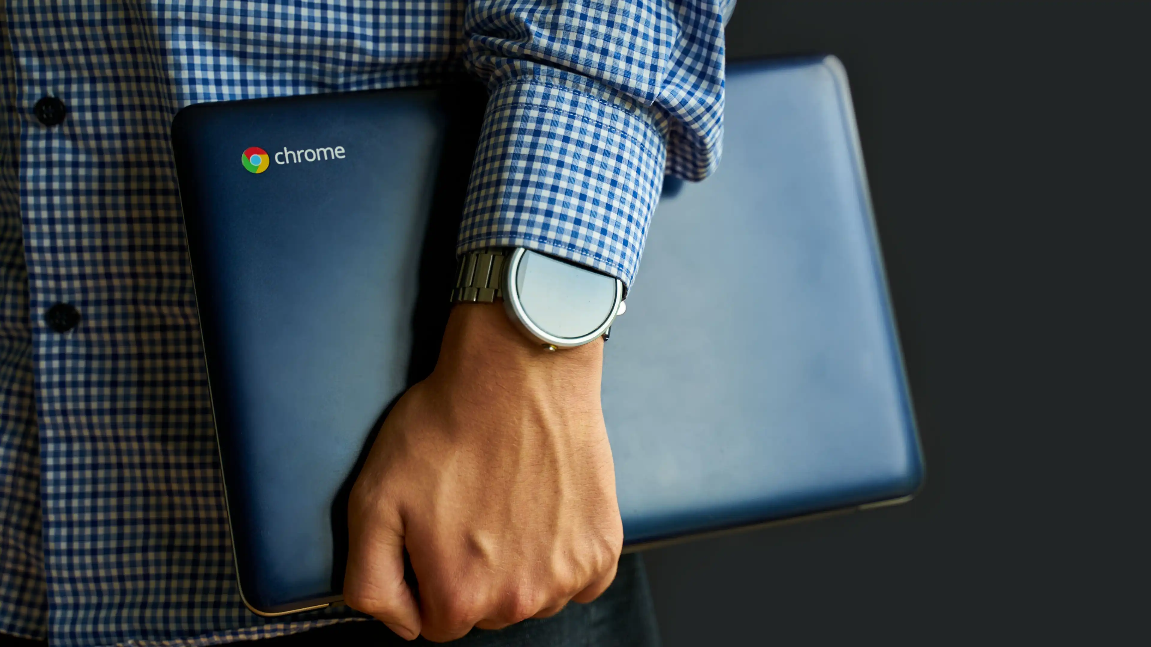 Eine Person im karierten Hemd trägt ein Chromebook mit Chrome-Logo unter dem Arm
