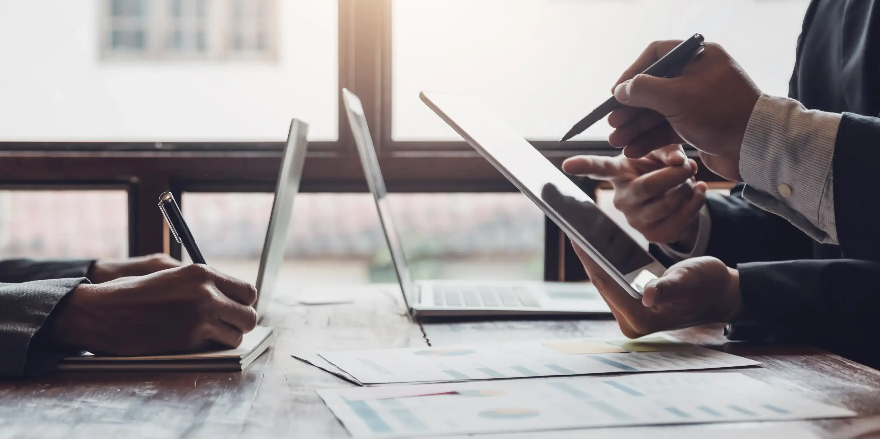 Tres personas están sentadas juntas en una mesa trabajando con varios dispositivos digitales