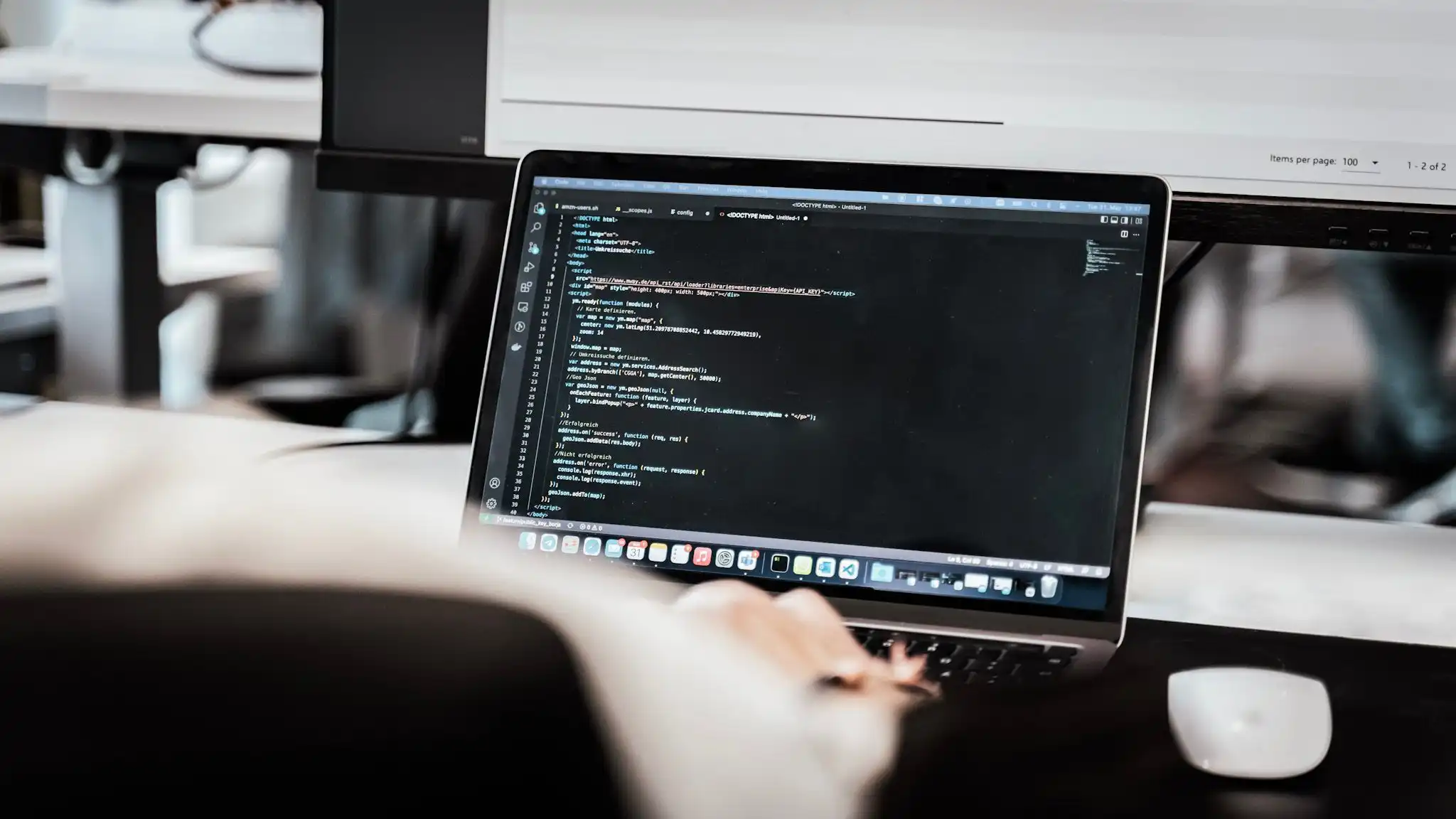 Eine Person sitzt an einem Schreibtisch und arbeitet an einem Mac, auf dem Bildschirm ist Programmcode zu sehen