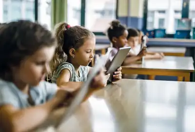 Jüngere Kinder in einem Klassenzimmer, alle haben jeweils ein Tablet in der Hand