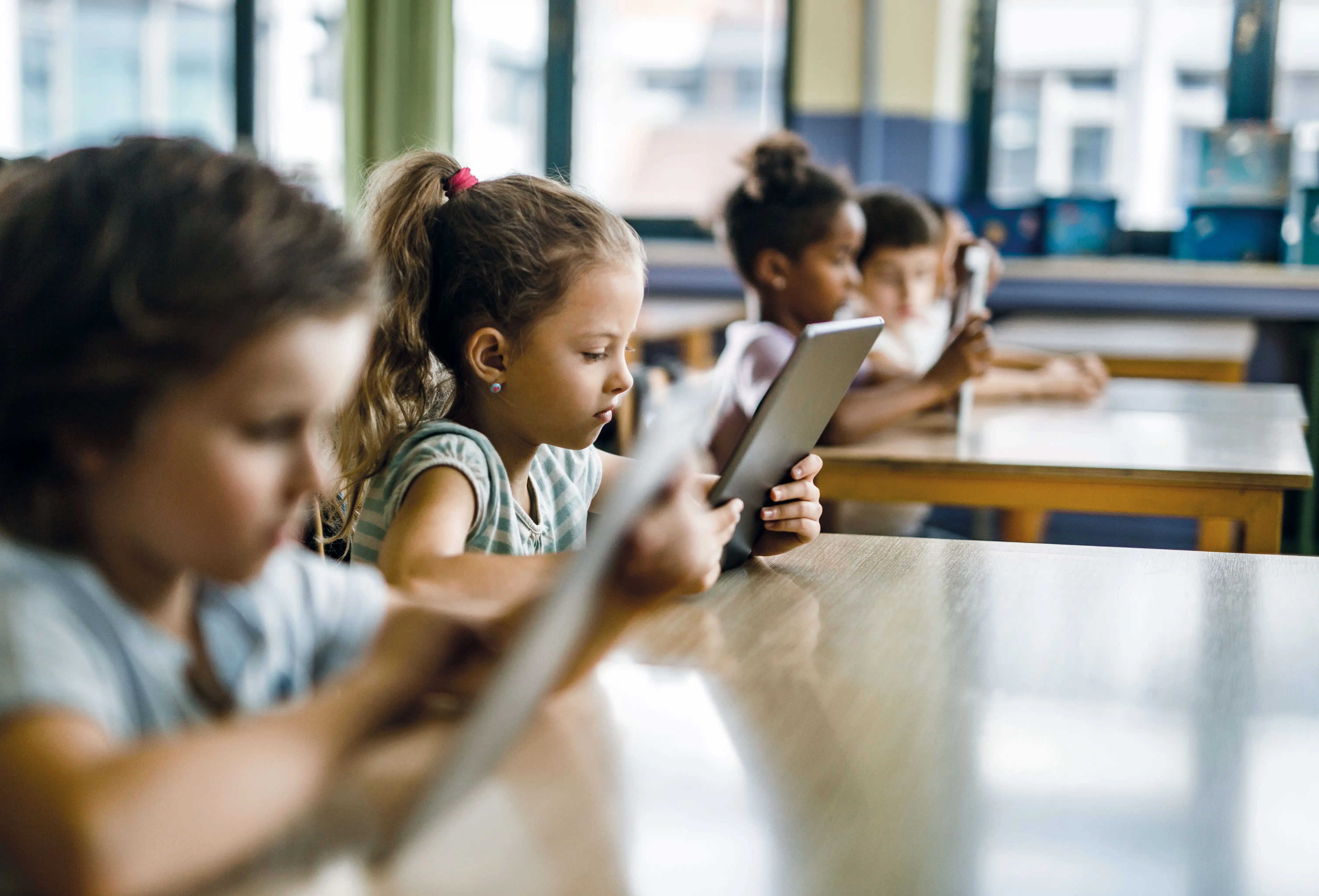 Younger children in a classroom each holding a tablet
