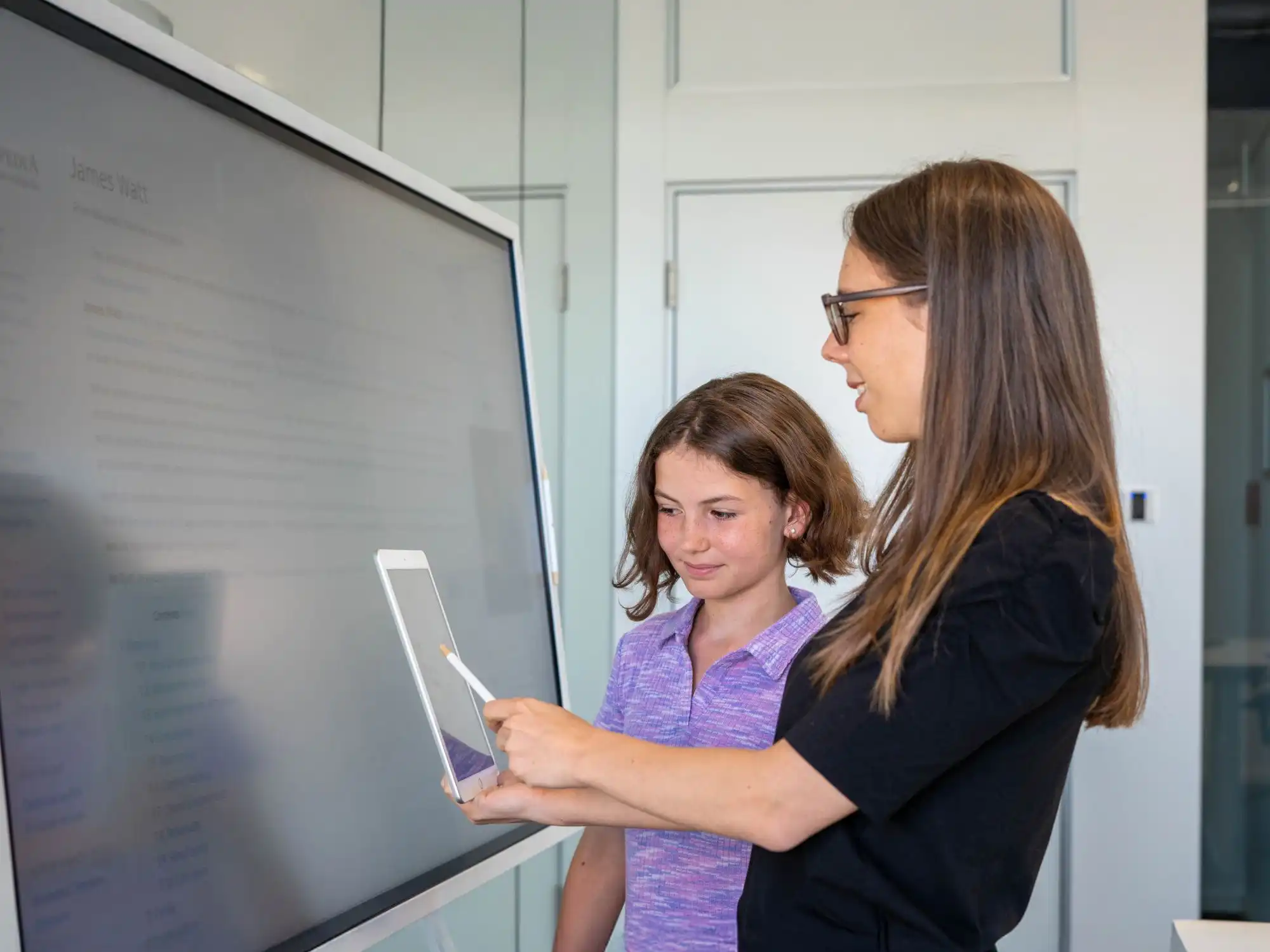 Eine Lehrerin und eine Schülerin arbeiten im Klassenzimmer gemeinsam an zwei digitalen Geräten