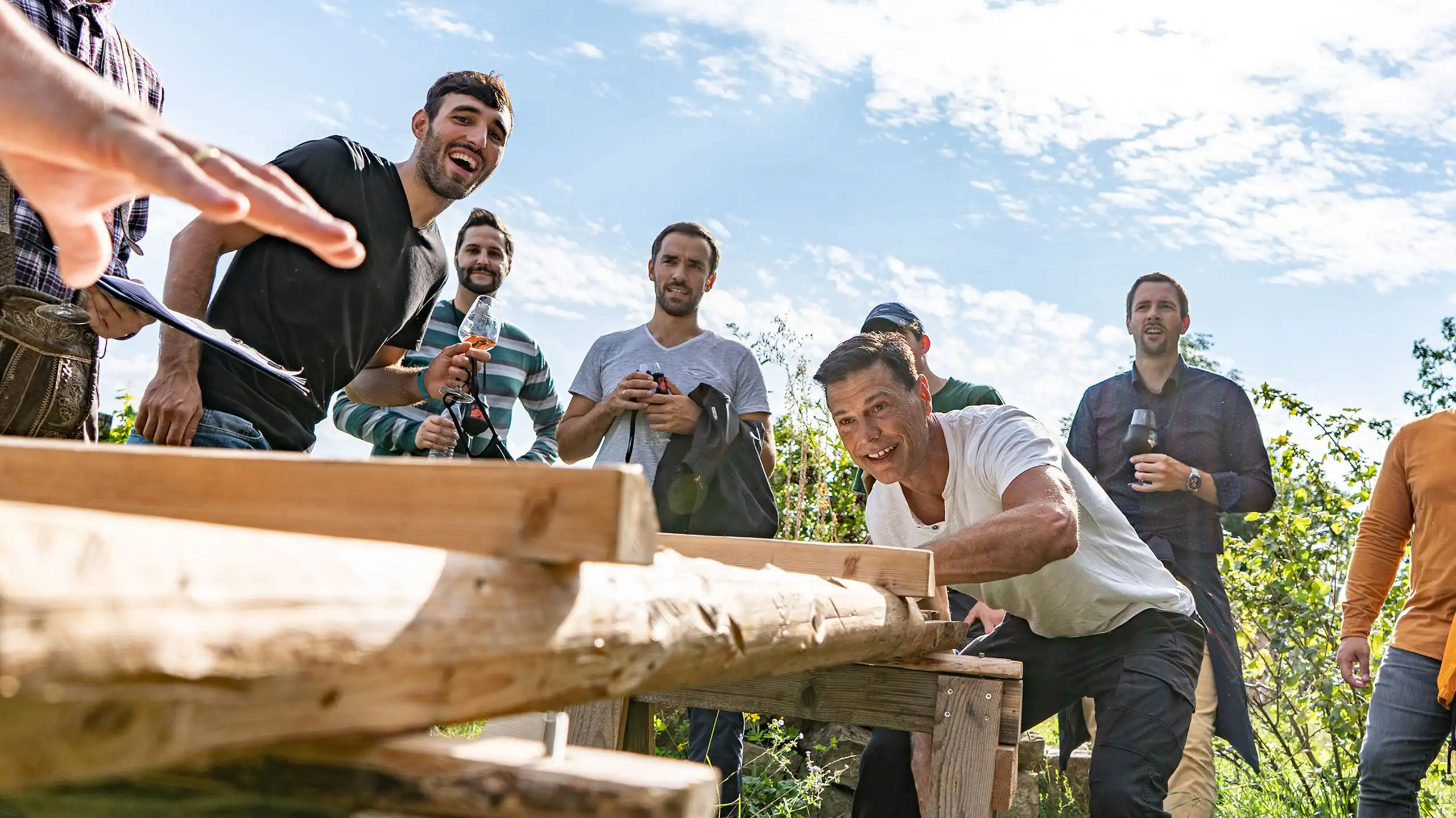 Eine Gruppe von Personen, die im Freien an einer Holzkonstruktion arbeiten, während sie lachen und miteinander interagieren.