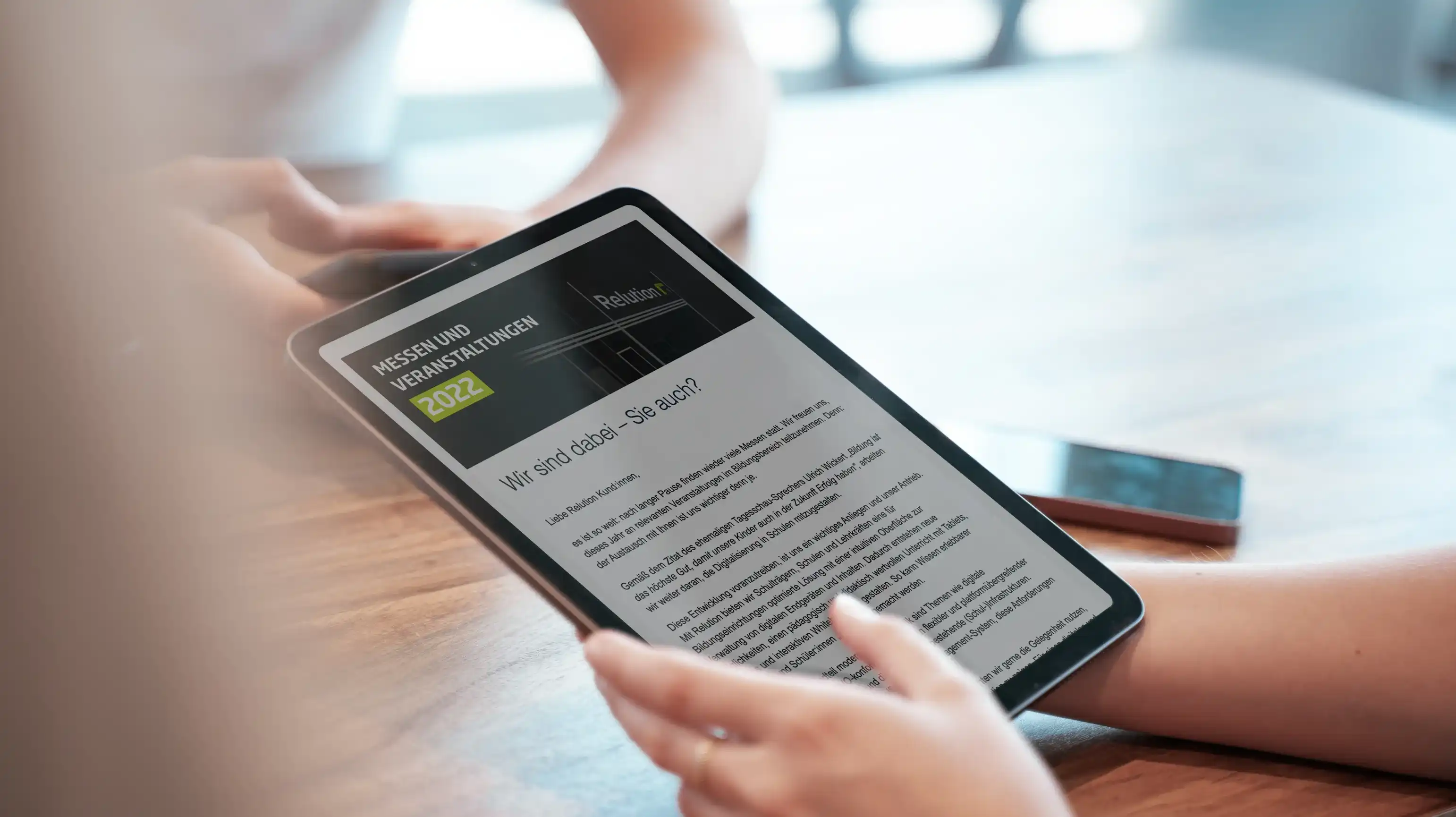 Una persona sostiene un iPad en su mano, mostrando un boletín informativo de Relution