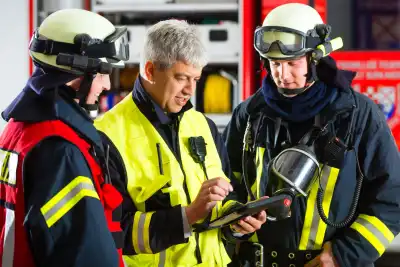 Drei Feuerwehrleute in Einsatzkleidung betrachten gemeinsam ein Tablet vor einem Einsatzfahrzeug