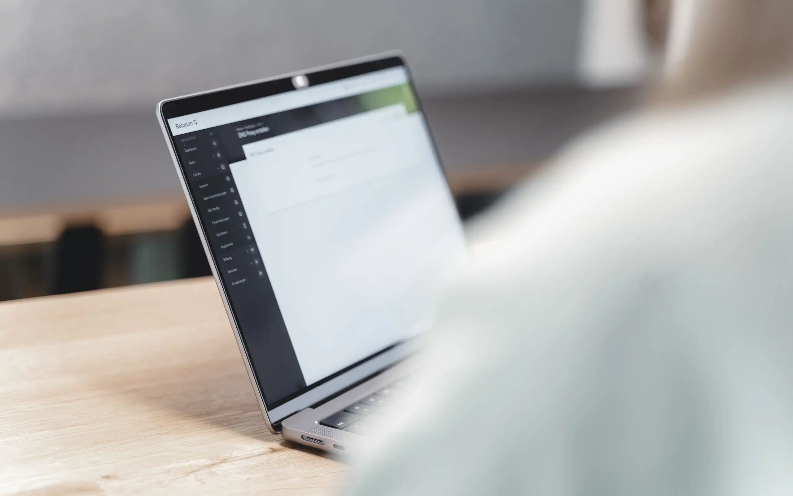 Un laptop è posizionato leggermente inclinato su un tavolo, una persona è seduta davanti, e l'app Relution è visibile sullo schermo