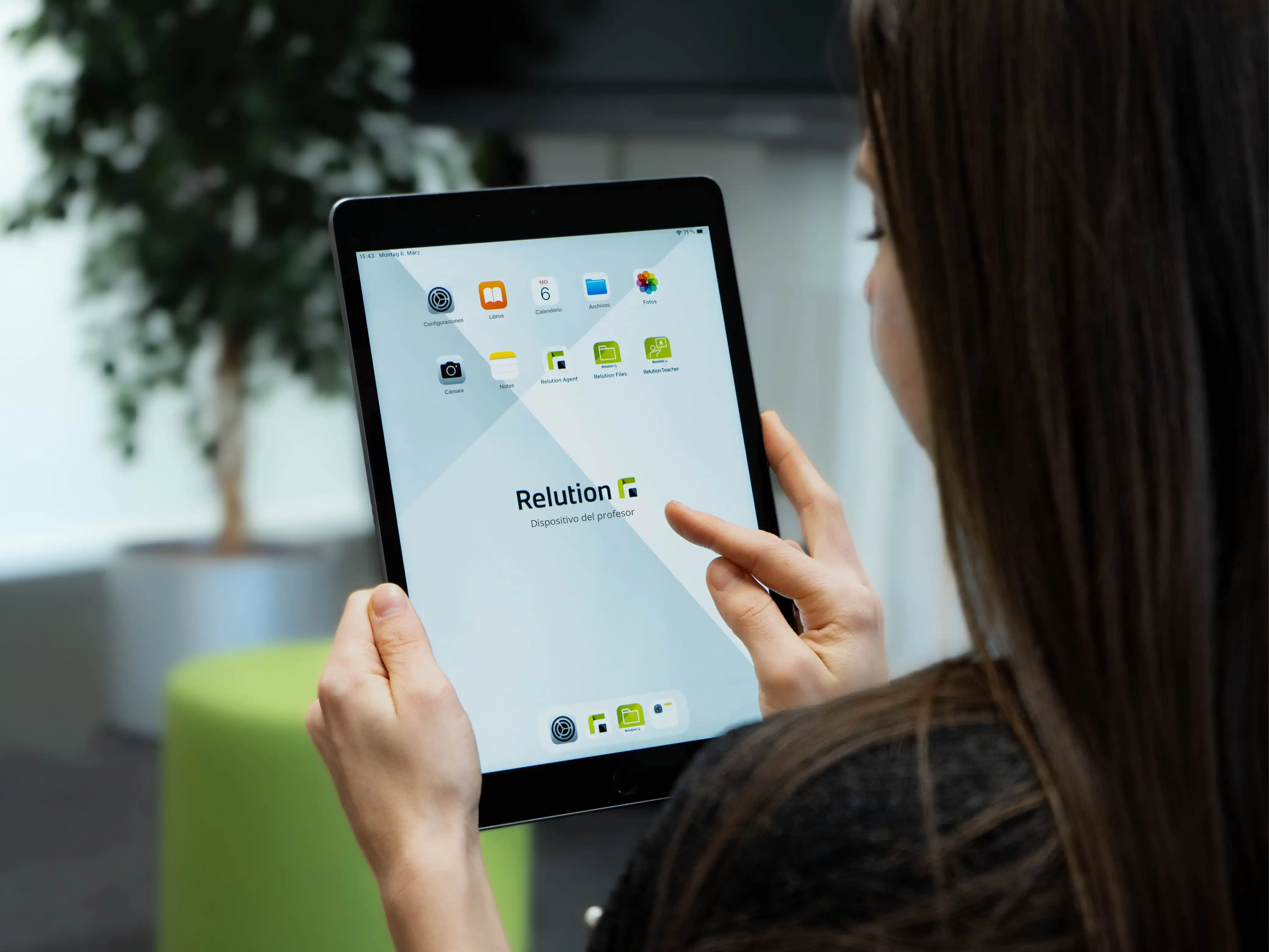 Una mujer sostiene un iPad en sus manos, mostrando la aplicación Relution Teacher junto con otros íconos de aplicaciones de Relution en la pantalla de inicio