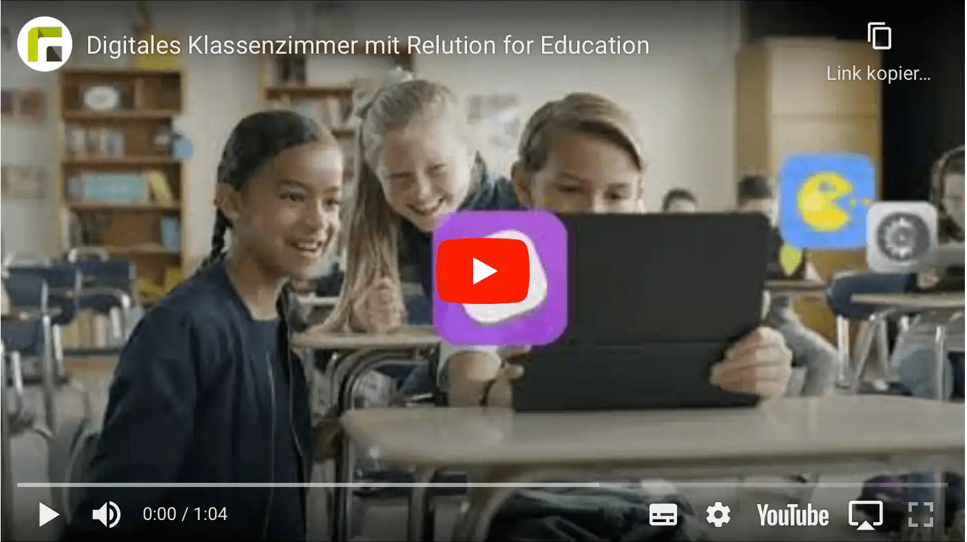 Three children are seen in a classroom in front of a shared tablet, while other children in the background are working on their tablets
