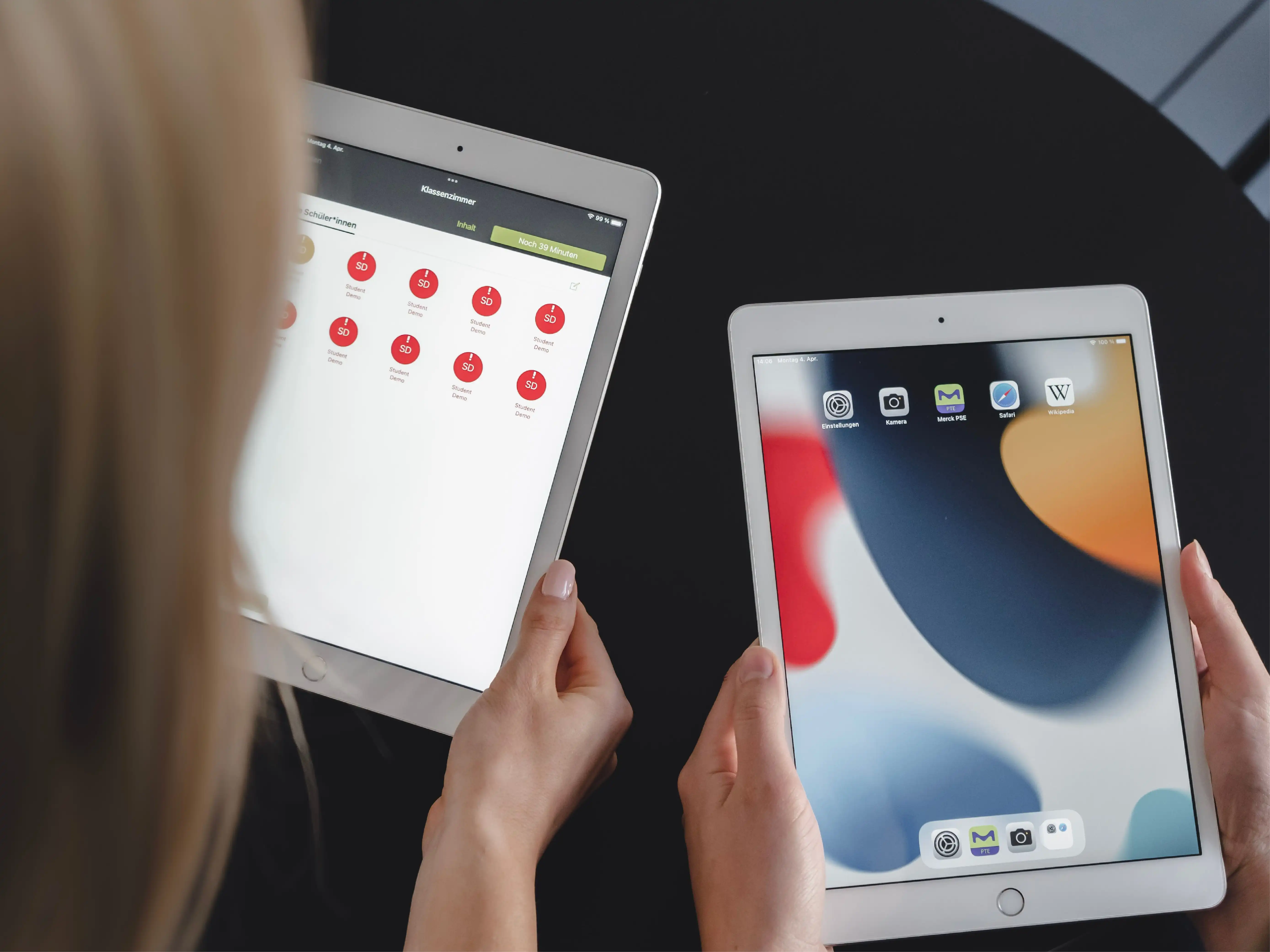 Two people are each holding a tablet, one showing the Relution Teacher App in use, the other displaying a preconfigured selection of apps