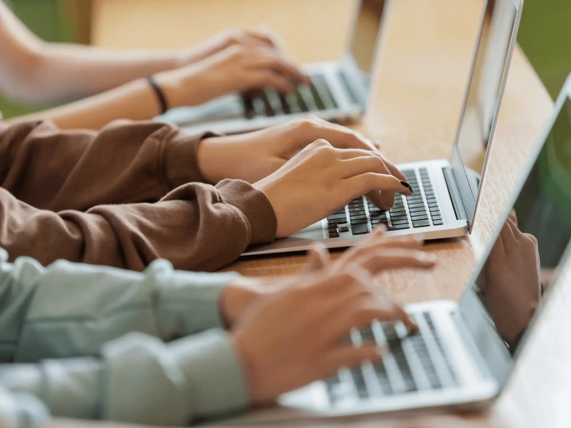 Zwei Personen arbeiten jeweils an ihrem Laptop, welche auf einem Holztisch stehen