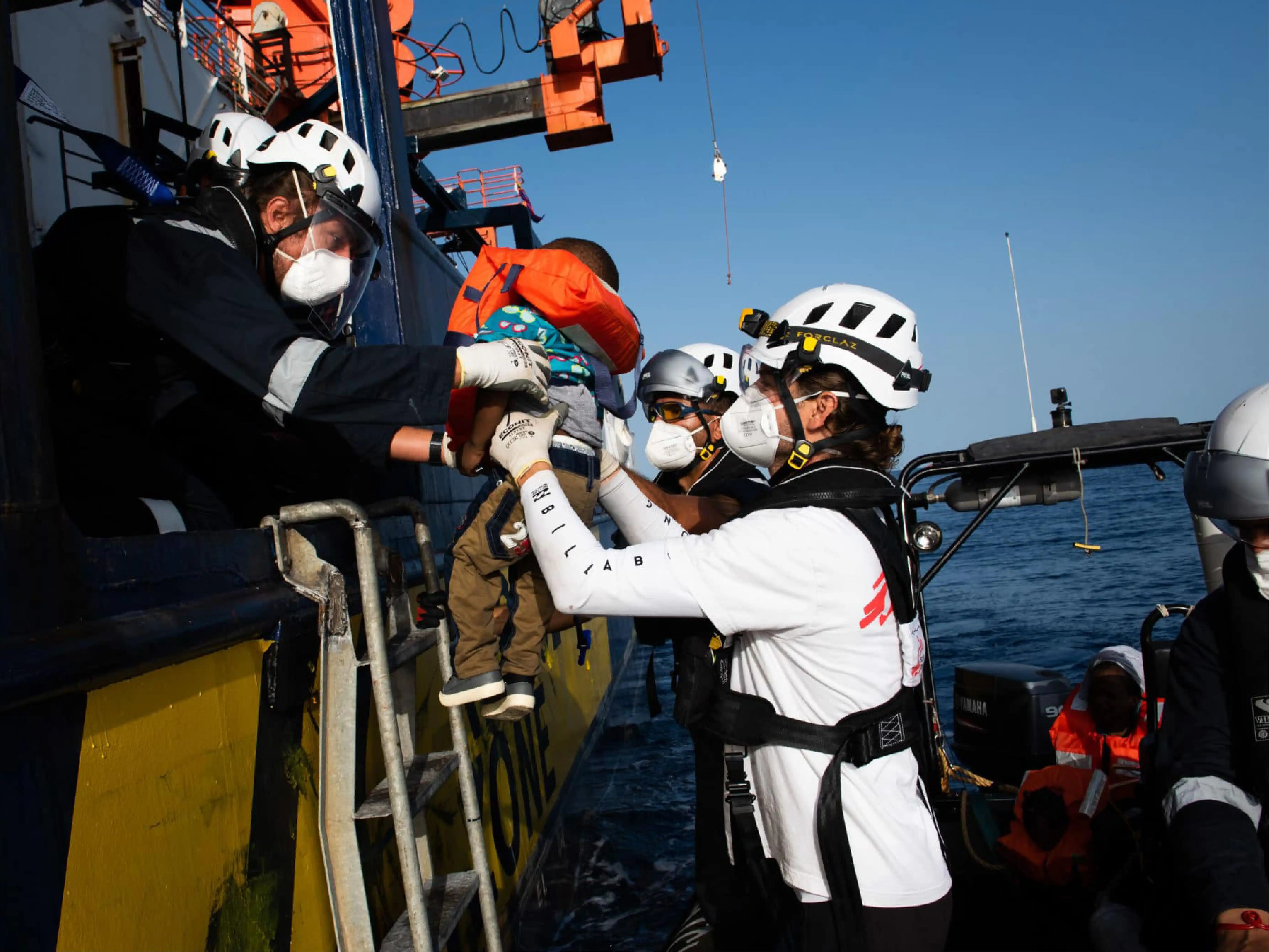 Members of Sea Watch lift a small child wearing a life jacket from a dinghy onto a larger ship