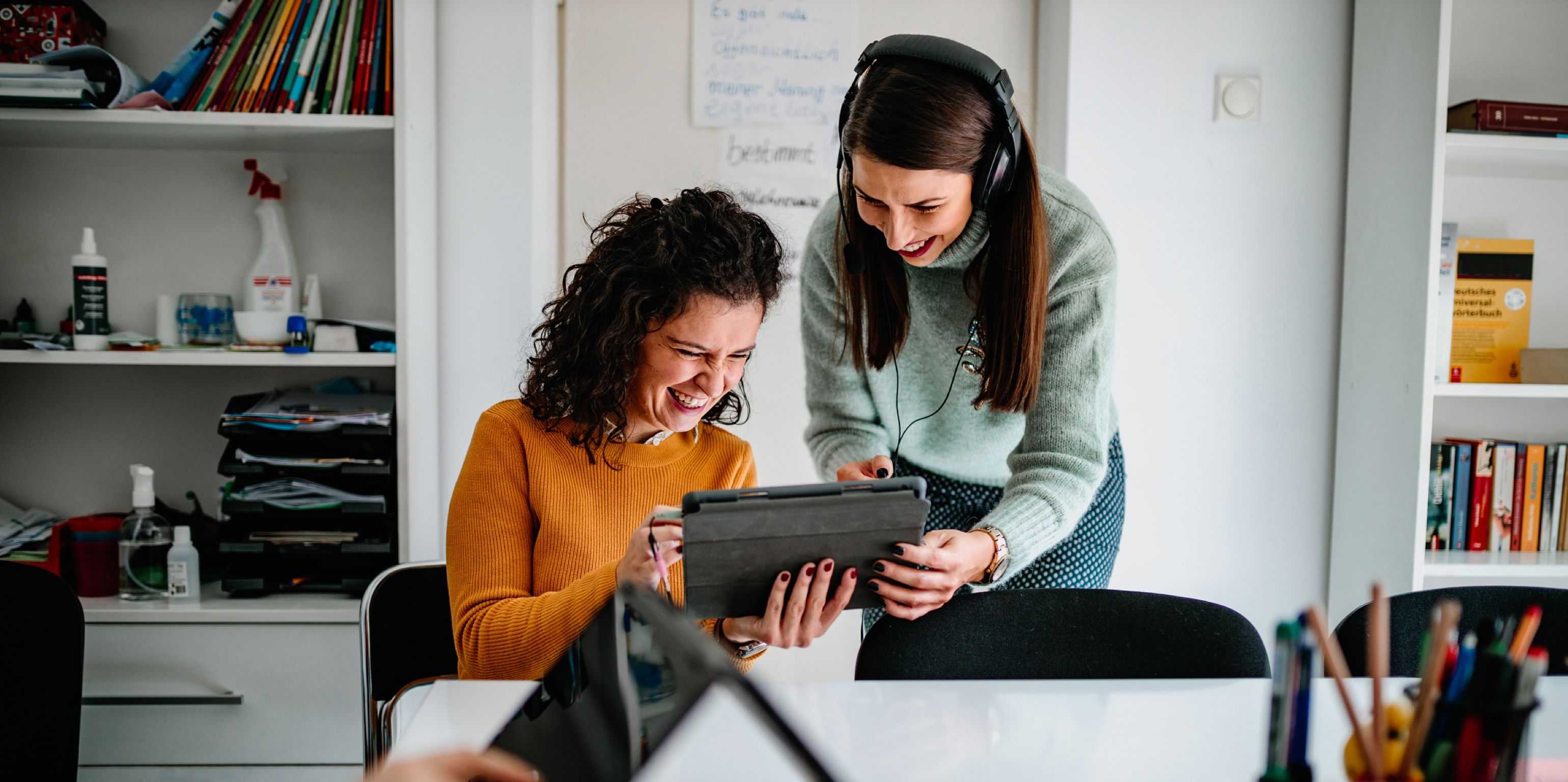 Zwei Frauen mit Kopfhörer werden vor einem Tablet angezeigt