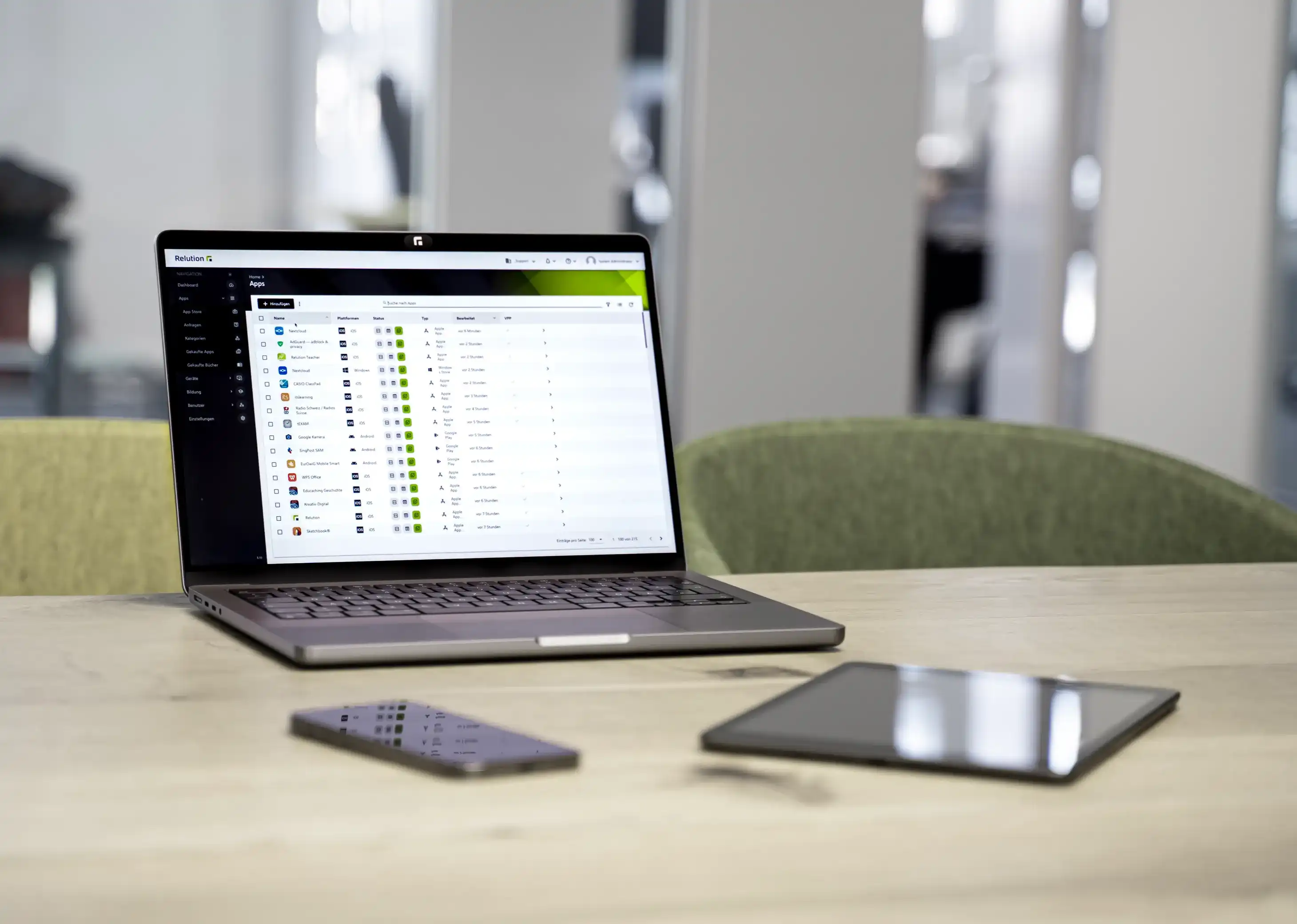 Various mobile devices are lying or standing on a table, with the layout of the Relution App visible on an open laptop