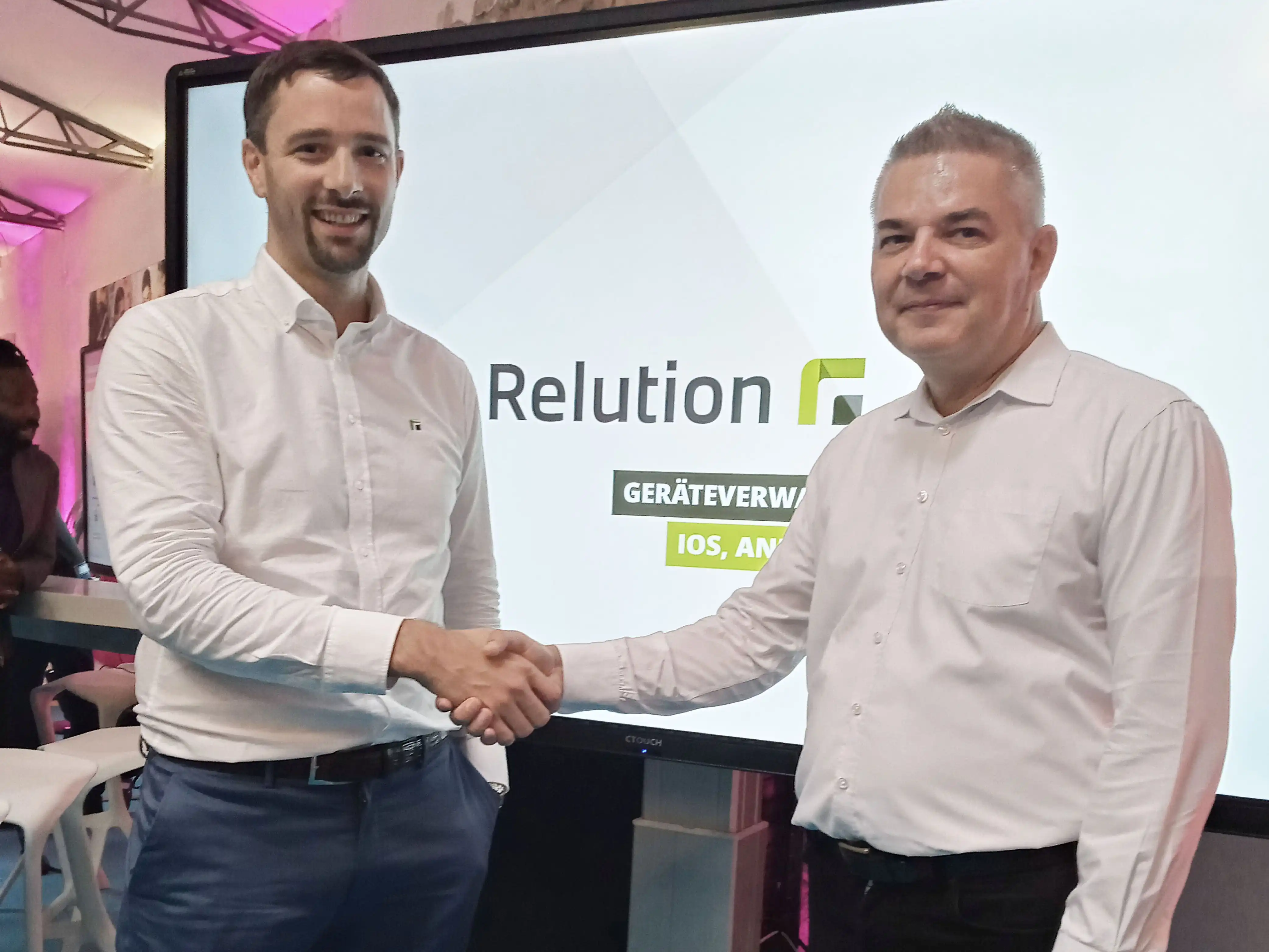 Moritz Mahlmann von Relution und Udo Wichert von E & W geben sich vor einem Whiteboard mit dem Logon von Relution die Hand