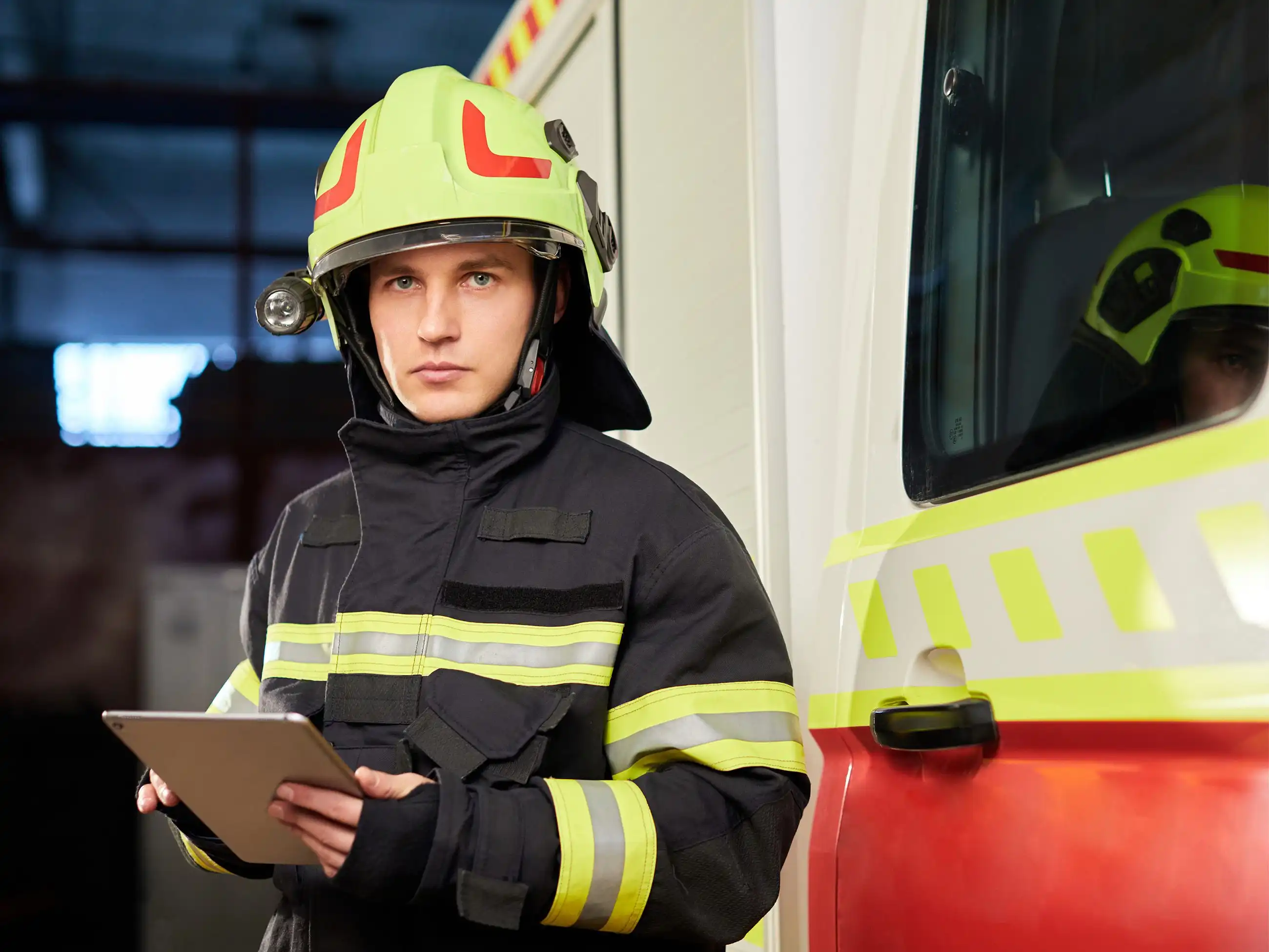 Ein Feuerwehrmann in voller Ausstattung steht neben einem Einsatzfahrzeug und hält dabei ein Tablet in seinen Händen