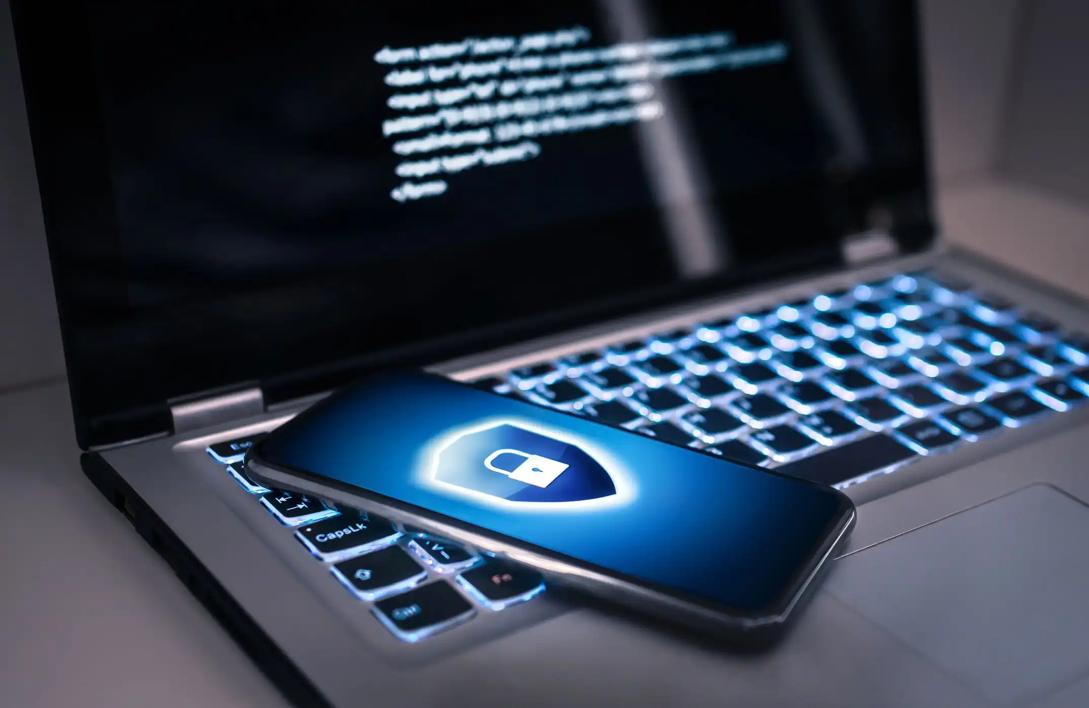 Ein Laptop, auf dessen Tasten ein Smartphone liegt, dessen Bildschirm ein Schild-Symbol mit einem geschlossenen Schloss zeigt.