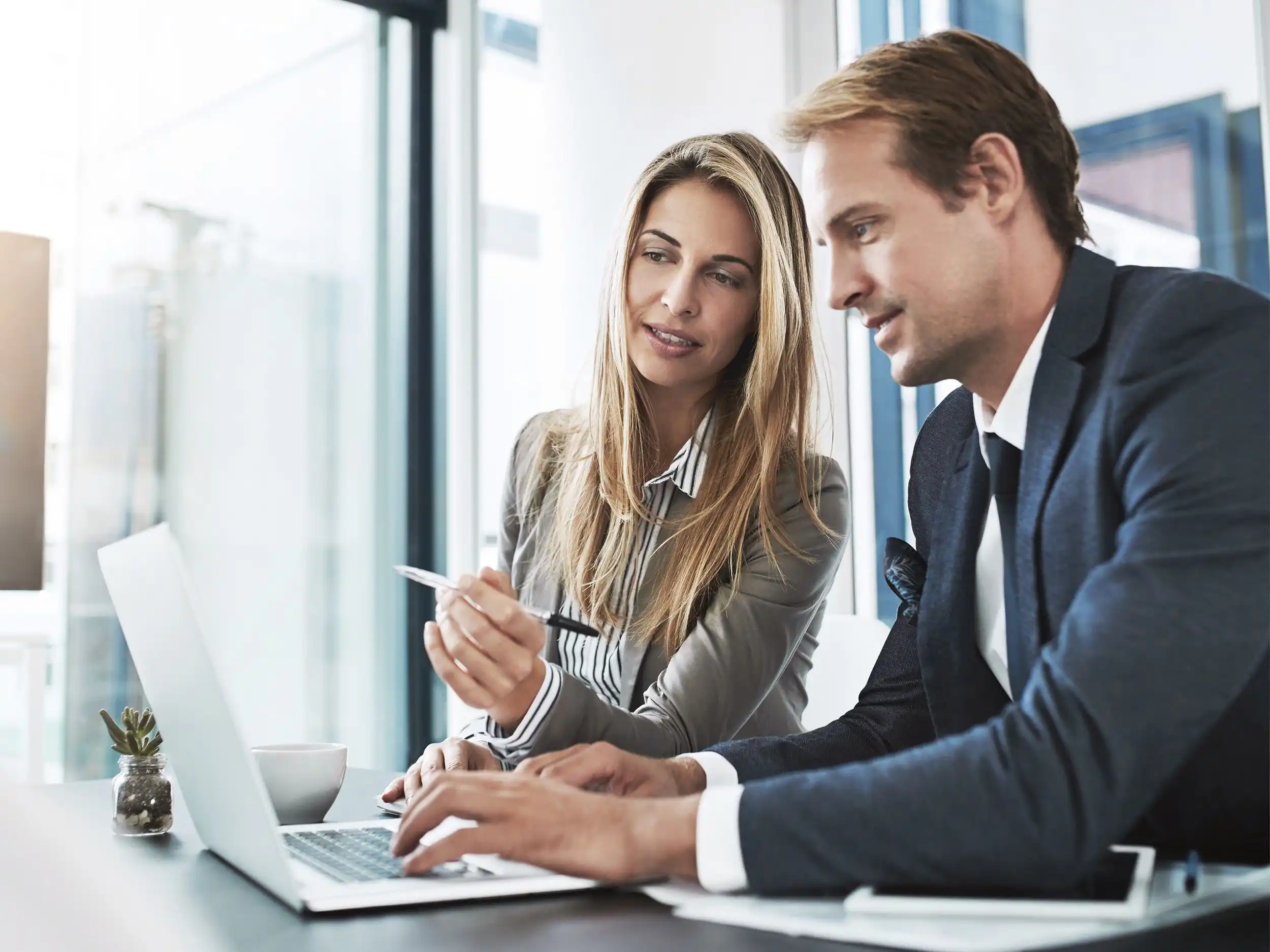 Eine Frau und ein Mann im Businesslook arbeiten gemeinsam an einem Laptop, in den beide konzentriert blicken