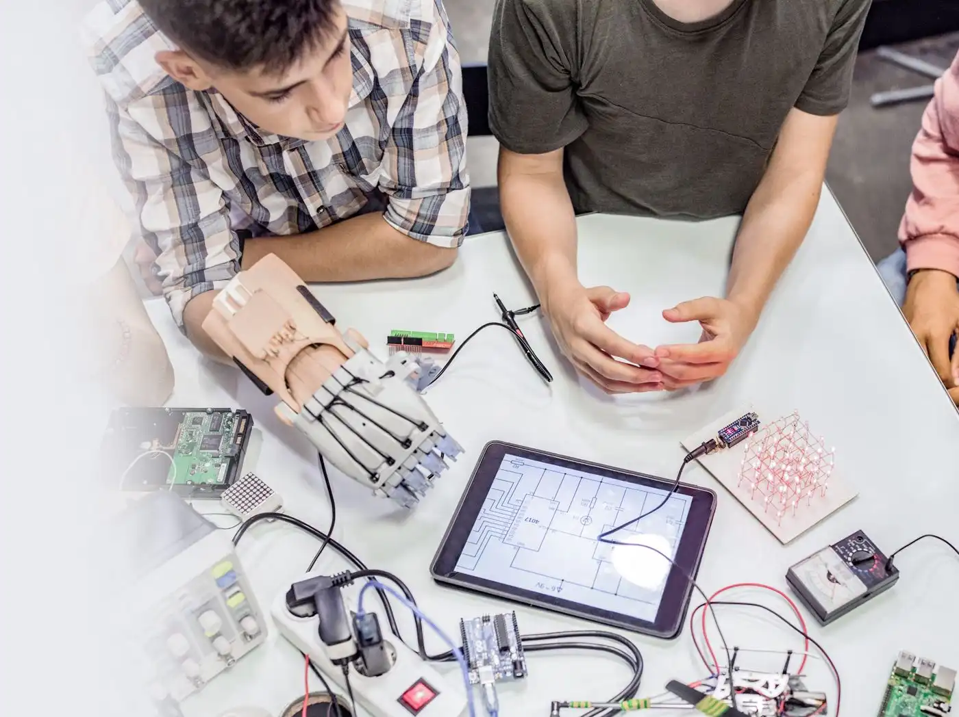 Trois jeunes personnes sont assises à une table avec de nombreux composants électroniques disposés autour d'une tablette affichant une sorte de schéma de circuit